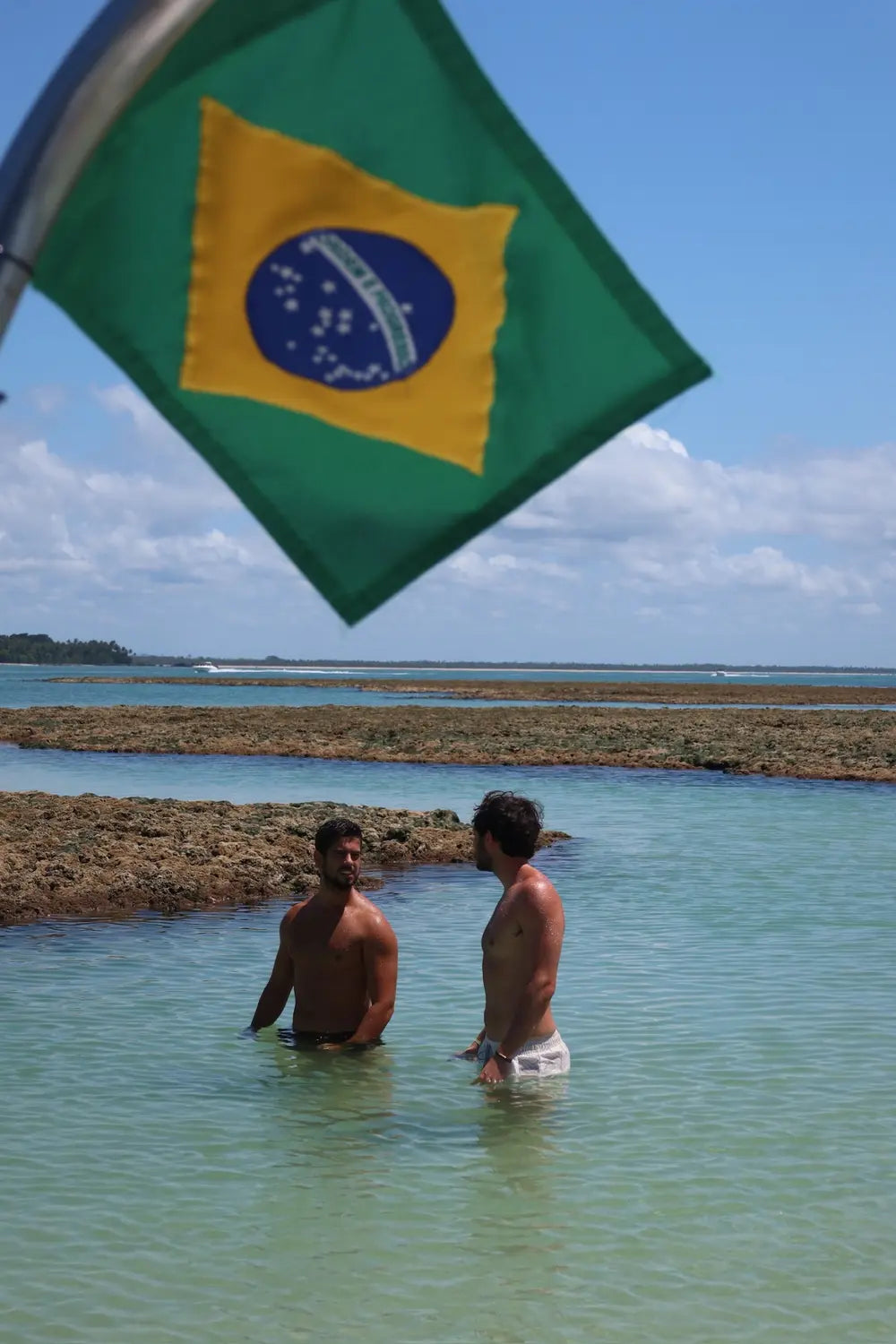 Elyse and Gabriel in the water beneath a Brazilian flag