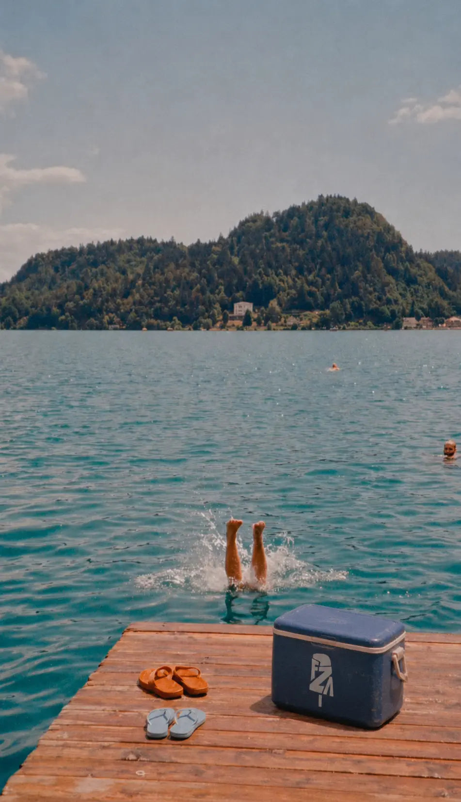A Freleza cooler on a dock beside a swimmer diving into the lake
