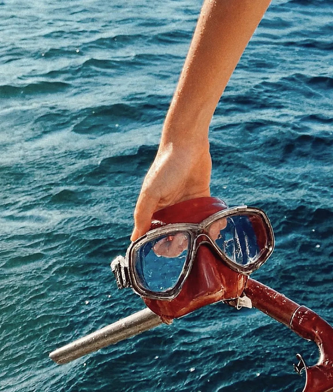 A red dive mask held above the ocean