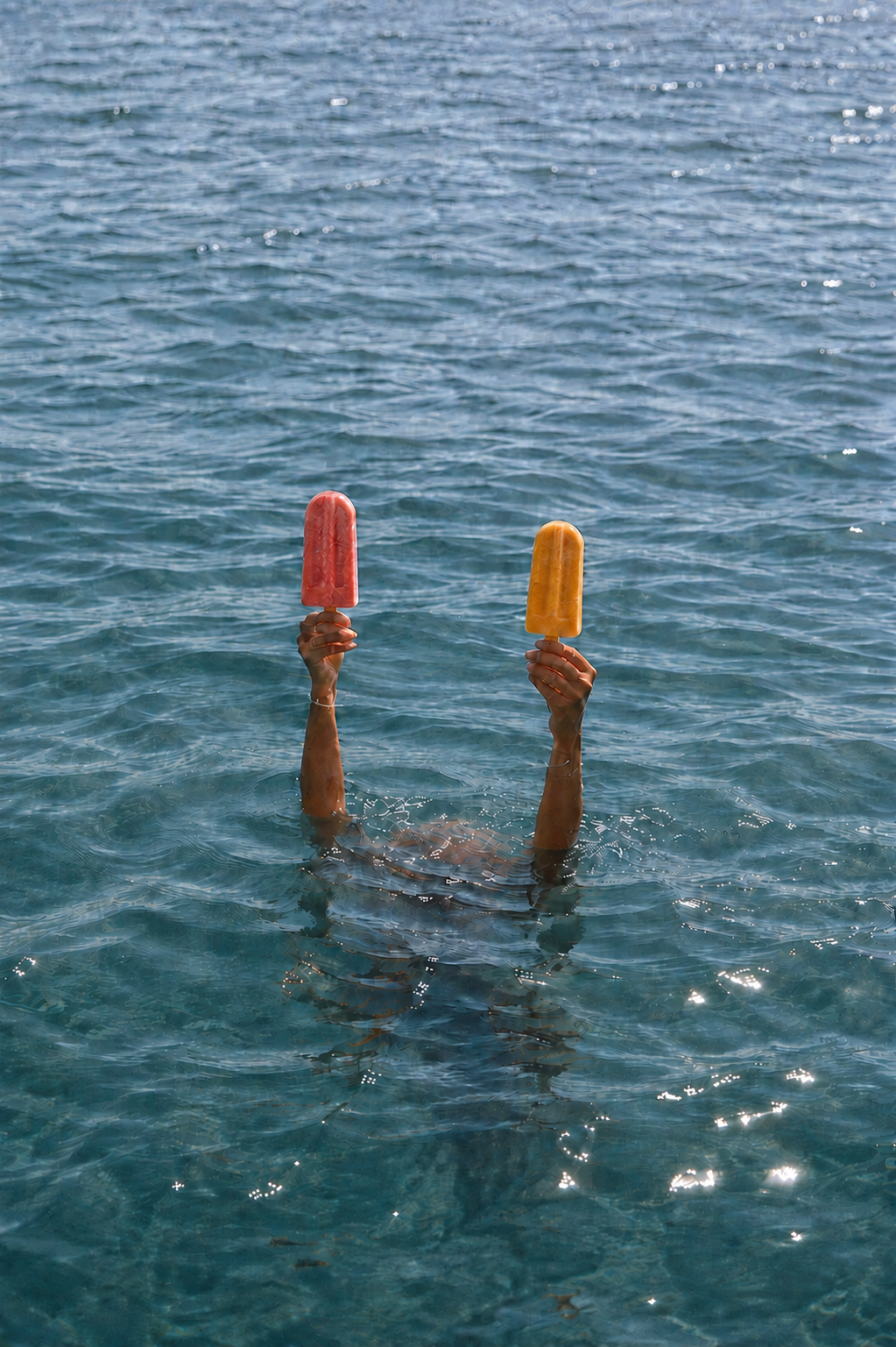 A swimmer holding two colorful frozen pops above the water